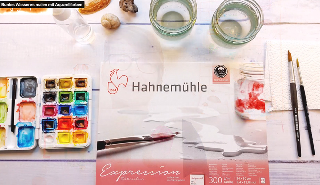 Malplatz mit Aquarellblock, Farbkasten, Pinseln, Wasserbechern