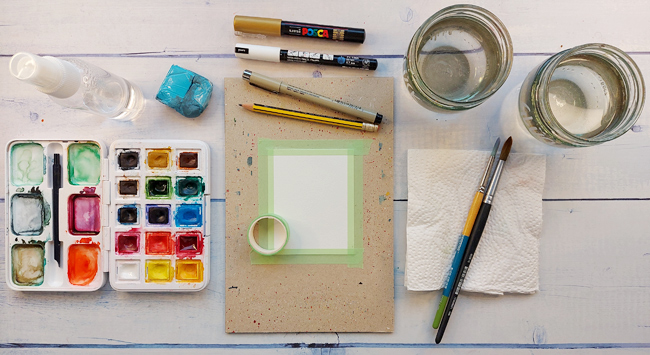 Aquarellfarbkasten, Pinsel, Papier, Wasserbecher auf Malplatz