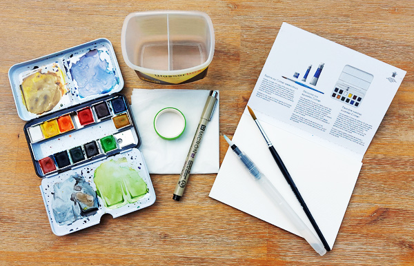 Kleines Aquarell-Set mit Farbkasten, Wasserbecher, Pinsel, Aquarellblock in Postkartengröße