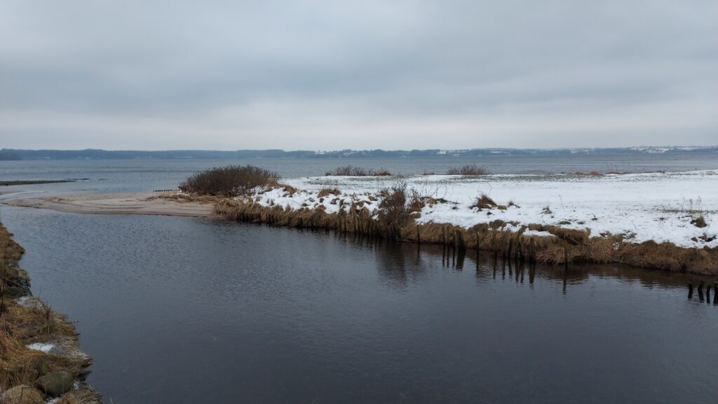 Kleine Landzunge mit Schnee umgeben von Wasser mit grauem Himmel