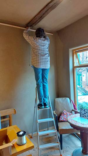 Frau auf Leiter befestigt was an Bilderaufhängungssystem