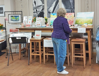 Frau kuckt Kunstdrucke an an Messestand