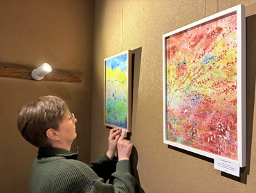 Frau klebt ein Infoschild auf den Bilderrahmen eines Aquarellbilds an einer Wand