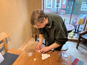 Frau beugt sich über Tisch und bearbeitet kleine weiße Preisschilder