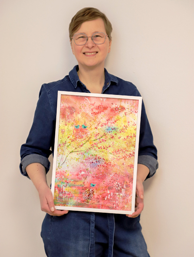 Frau in blauem Overall mit Aquarellbild in den Händen