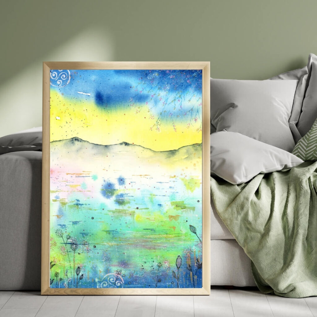 Aquarell-Kunstdruck abstrakt in Blau, Gelb und Türkis in hellem Rahmen auf Boden vor einem hellen Schlafsofa mit Kissen und Decken