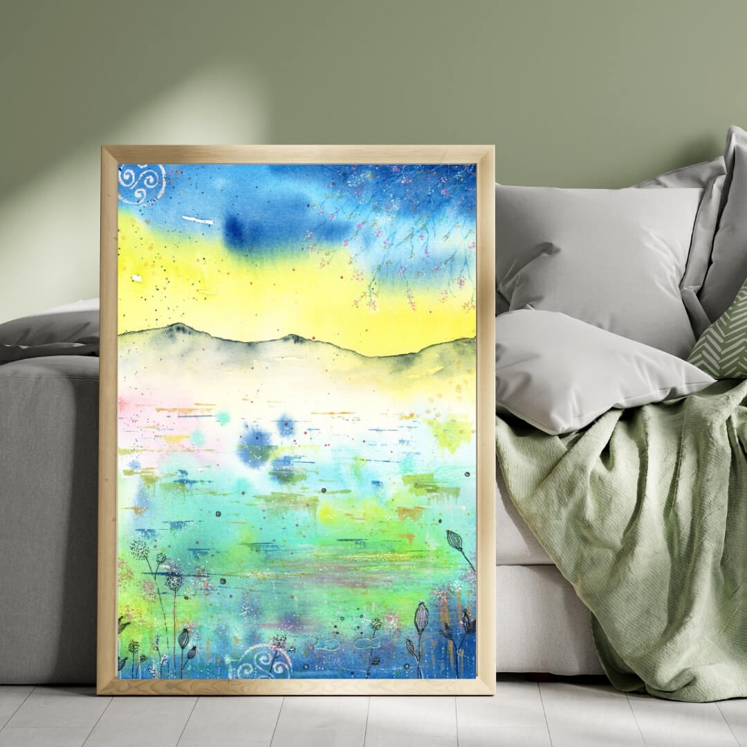 Aquarell-Kunstdruck abstrakt in Blau, Gelb und Türkis in hellem Rahmen auf Boden vor einem hellen Schlafsofa mit Kissen und Decken