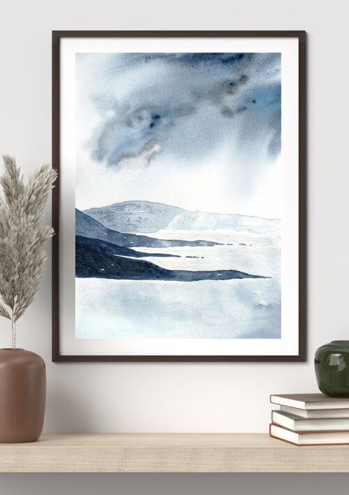 Aquarell-Kunstdruck mit schwarzen Küstenfelsen und grauen Sturmwolken an heller Wand über Regalbrett