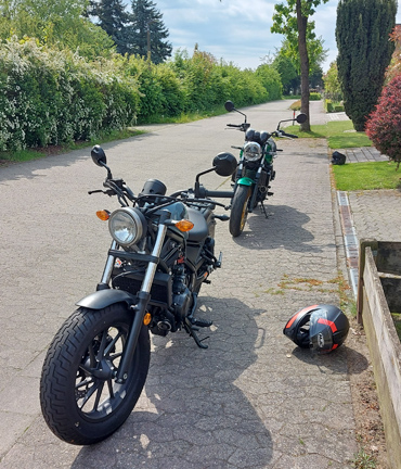 zwei Motorräder parken hintereinander in schmaler begrünter Straße