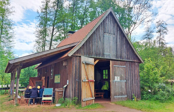 rustikales Holzhaus mit rotem Dach und grünen Bäumen dahinter