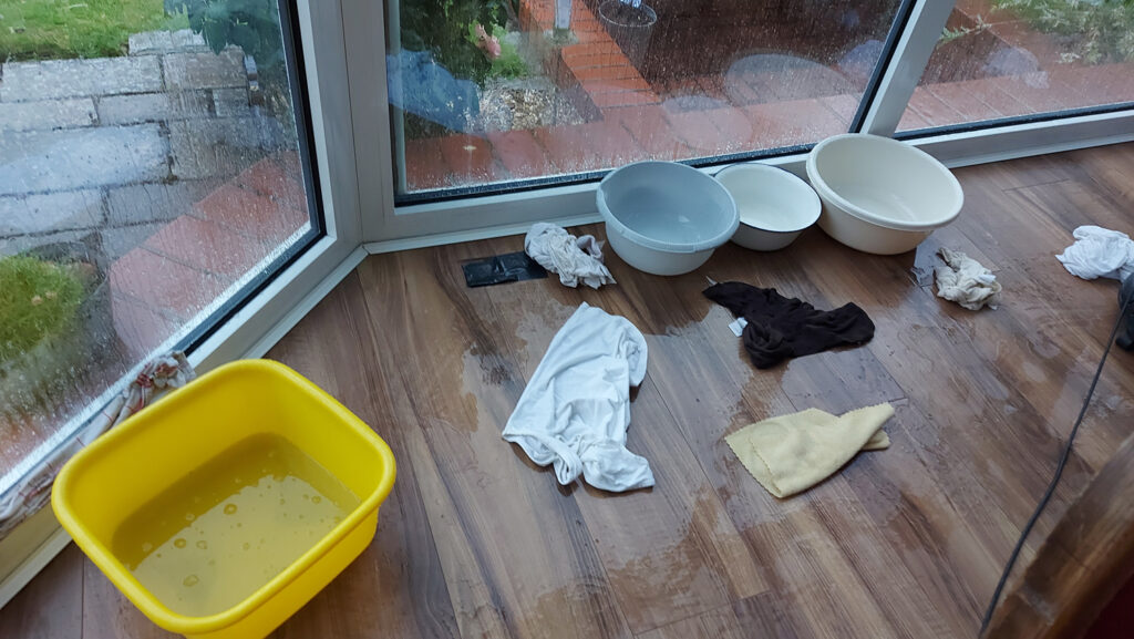Schüsseln, Lappen und Wasser auf dunklem Laminatfußboden