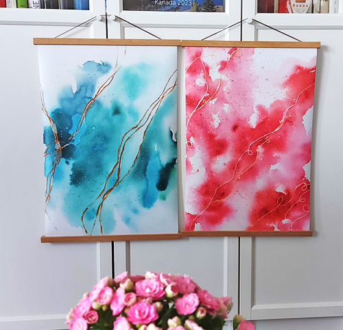 Zwei Aquarell-Poster eins in Blau eins in Rot aufgehängt mit Posterleisten aus hellem Holz