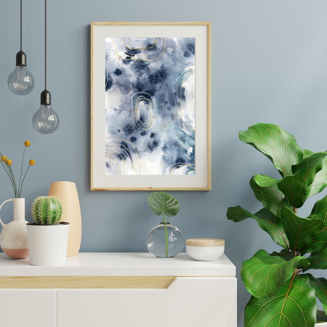 Abstraktes Aquarell in Grautönen vor grauer Wand über hellen Möbeln mit Grünpflanze