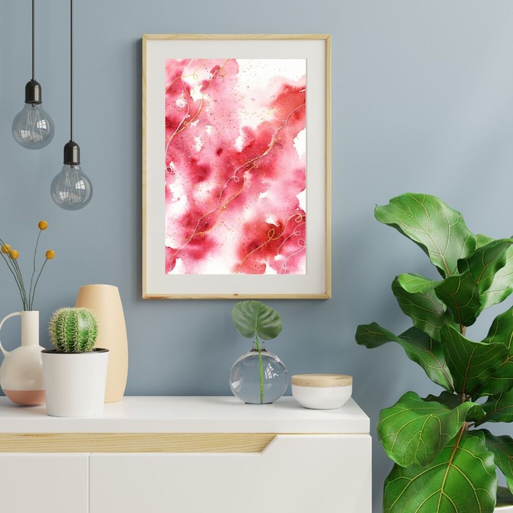 Abstraktes Aquarell in Rottönen an grauer Wand über weißem Möbel daneben Grünpflanze