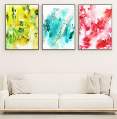 Drei abstrakte Aquarell-Kunstdrucke in blau, rot, grün über hellem Sofa