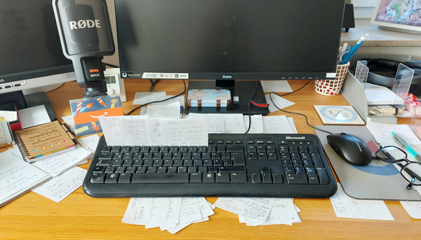 Schreibtisch mit PC-Bildschirm, Tastatur, vielen Zetteln