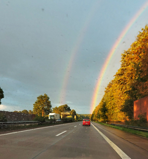 Blick aus Auto-Frontscheibe auf einen Doppel-Regenbogen voraus