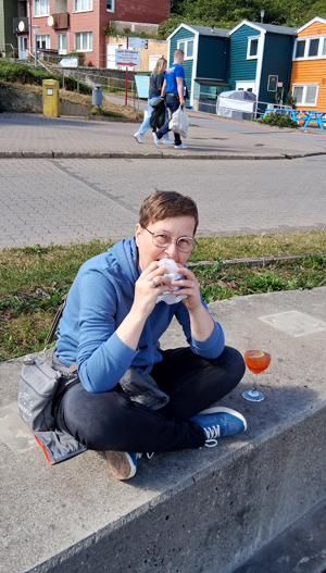 Frau isst Fischbrötchen sitzend auf Mauer